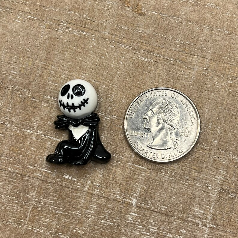May include: Black and white Jack Skellington charm with a black bow tie and cape. The charm is about the size of a US quarter.