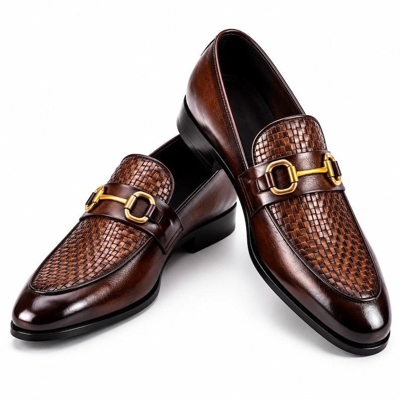 Pode incluir: Um par de mocassins de couro castanho escuro com uma textura entran&ccedil;ada no peito do p&eacute; e um detalhe de brid&atilde;o em metal dourado no topo. Os sapatos t&ecirc;m um acabamento em couro liso nas laterais e um salto baixo preto, apresentados em &acirc;ngulo.