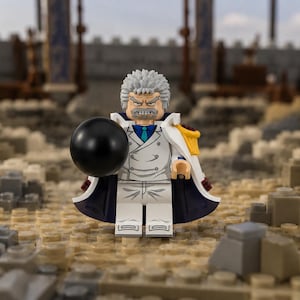 Puede incluir: Una minifigura de plástico que representa a un personaje con cabello gris puntiagudo, barba gris y una expresión facial severa. La figura viste un abrigo blanco de doble botonadura con corbata azul, una capa blanca con detalles amarillos y sostiene una esfera negra.