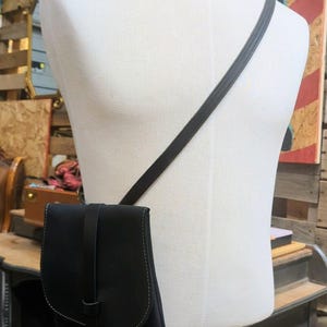 May include: A black leather crossbody bag with a long strap. The bag has a flap closure and a small pocket on the front.