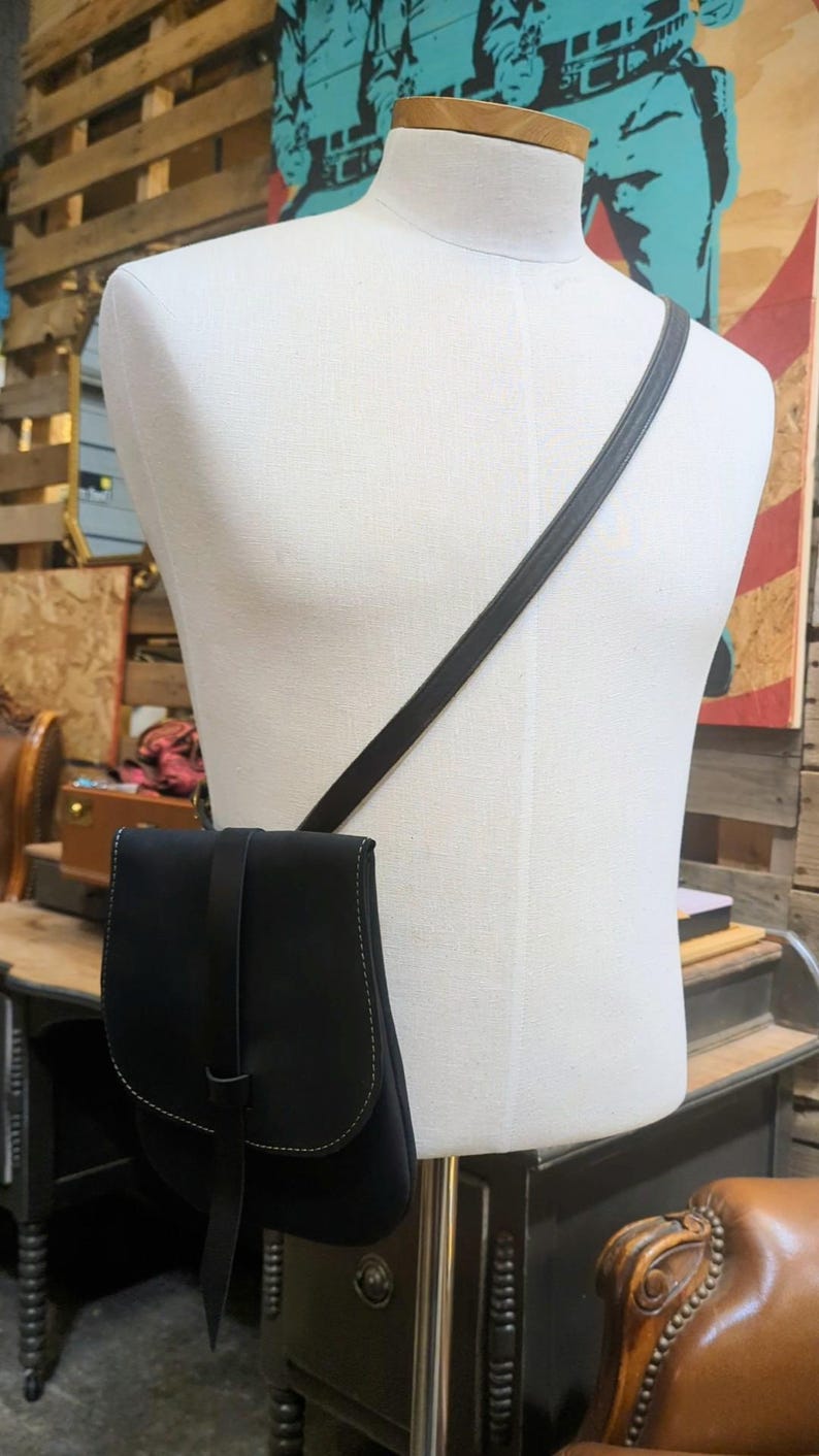 May include: A black leather crossbody bag with a long strap. The bag has a flap closure and a small pocket on the front.