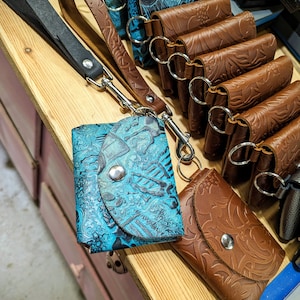 May include: A collection of leather keychains with intricate designs. The keychains are brown and blue with a variety of patterns. The keychains are attached to a metal ring and a leather strap.