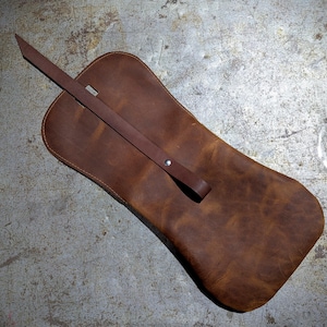 May include: A brown leather pouch with a flap closure and a long strap. The pouch is made of distressed leather and has a rustic look.