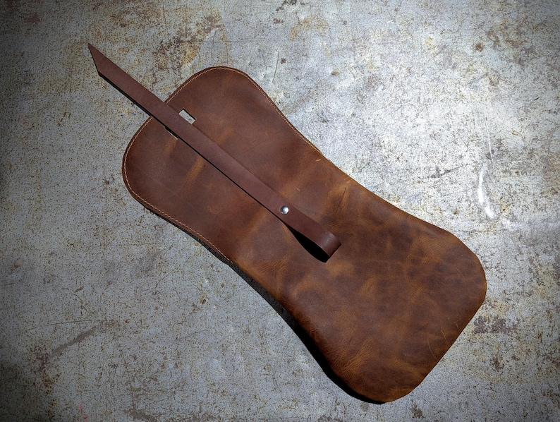 May include: A brown leather pouch with a flap closure and a long strap. The pouch is made of distressed leather and has a rustic look.