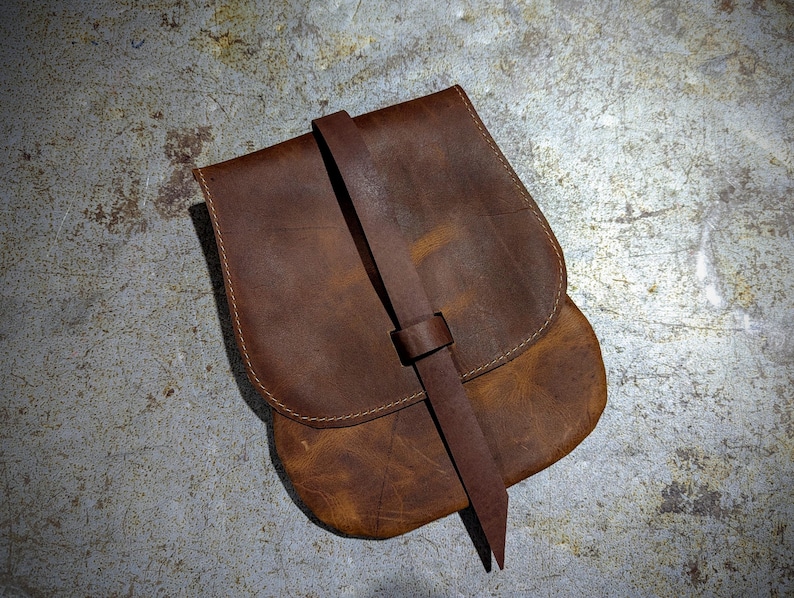 May include: A brown leather satchel with a long strap. The bag has a flap with a buckle closure and is made of distressed leather.