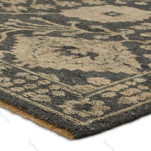 May include: A rectangular area rug featuring a dark charcoal gray background with a contrasting beige floral pattern. The rug has a woven texture and a short fringe along the edge. The text Nafisa Rug Store is visible in the lower corner area.