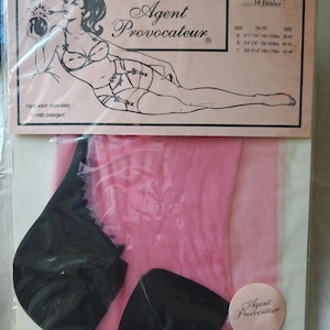 May include: A package of pink 15 denier 100% nylon stockings by Agent Provocateur. The packaging features a black and white illustration of a person in lingerie holding a bomb, with a size chart listing heights in feet and weights in pounds.