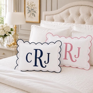 Peut inclure: Deux coussins décoratifs rectangulaires blancs à bords festonnés. Le coussin avant présente un monogramme brodé bleu marine avec les lettres cRJ. Le coussin arrière présente un monogramme brodé rose avec les lettres RJ.
