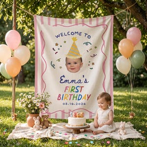 May include: A rectangular fabric banner featuring a pink striped border and the text "WELCOME TO Emma's FIRST BIRTHDAY 16.08.2026". The centre displays a graphic of a baby wearing a yellow party hat surrounded by colourful confetti and star shapes.