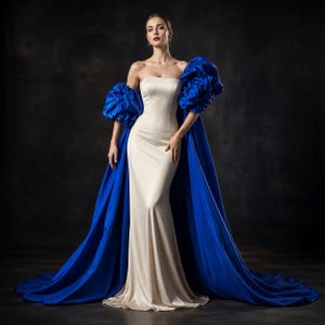 May include: A floor-length, strapless cream-colored gown featuring a smooth, fitted bodice and skirt. The dress is accented by voluminous, detachable royal blue puff sleeves that extend into a long, flowing train trailing behind the garment.