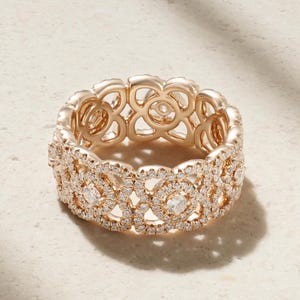 Könnte beinhalten: Ein Ring aus Roségold mit einem komplizierten durchbrochenen Design aus sich wiederholenden floralen Motiven. Die Oberfläche des Metalls ist mit zahlreichen kleinen, klaren, rund geschliffenen Diamanten besetzt, die den Konturen folgen.