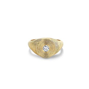 Könnte beinhalten: Ein goldener Siegelring mit einer texturierten Oberfläche und konzentrischen, kreisförmigen Rillen, die von der Mitte ausstrahlen. Ein einzelner, klarer, rund geschliffener Edelstein ist sicher in der Mitte des Rings gefasst.