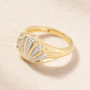 Könnte beinhalten: Ein goldener Ring mit einem muschelförmigen Design, das abwechselnd glatte Goldrippen und vertiefte Kanäle aufweist, die mit kleinen, klaren, funkelnden Steinen besetzt sind. Das Band besteht aus poliertem Gold und erinnert an eine Muschel.