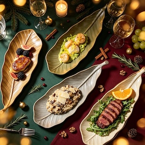 May include: Four elongated leaf-shaped serving platters in shades of gold, light green, and off-white, each holding a different gourmet dish including seared scallops, sliced duck breast, mushroom risotto, and a fruit-topped pastry on a festive table.