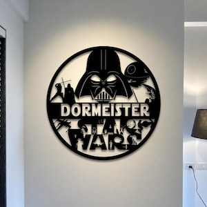 Pode incluir: Uma placa de parede circular preta com um design recortado de Darth Vader, a Estrela da Morte e várias naves espaciais. O texto "DORMEISTER" é exibido numa barra horizontal no centro, com as palavras "STAR WARS" posicionadas abaixo.