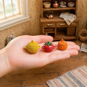 May include: Three miniature lidded containers shaped like food items: a yellow spiky durian, a red tomato with a green stem, and an orange pumpkin. Each small vessel features two side handles and a rounded body, designed for decorative display.