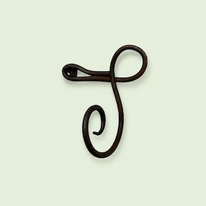 Puede incluir: Un gancho de pared de metal forjado a mano en color marrón oscuro con un diseño curvo en forma de S. El gancho tiene un acabado liso y redondeado con un orificio de montaje circular visible en el extremo superior izquierdo.
