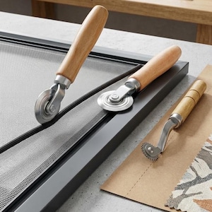 May include: Three screen installation tools with light-colored wooden handles and metal components. Two tools feature smooth circular wheels for pressing spline into a black window screen frame, while the third tool has a serrated wheel.