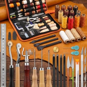 May include: A leather crafting kit featuring a black zippered organizer case filled with various spools of thread, needles, and metal tools. Includes a metal ruler, stitching chisels, awls, punches, scissors, and a craft knife on a leather surface.