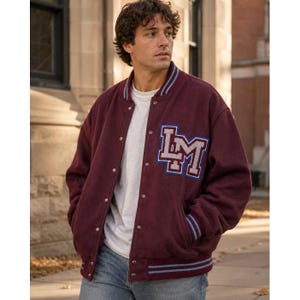 May include: A burgundy varsity jacket featuring a white and blue lettered patch with the initials LM on the left chest. The jacket has a snap-button front closure, long sleeves with ribbed cuffs, and a ribbed hem with blue and white striped detailing.