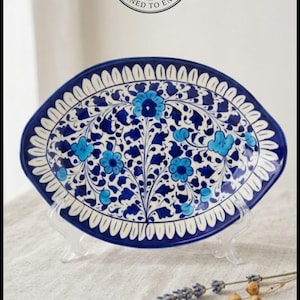 May include: An oval ceramic platter featuring a deep blue and white floral pattern with bright blue accents. The border has a repeating white leaf motif. A circular logo at the top reads M&F CRAFT CO, CRAFTED BY HAND, DESIGNED TO ENDURE.