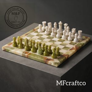 Puede incluir: Un juego de ajedrez cuadrado con tablero y piezas talladas en piedra pulida. El tablero muestra una cuadrícula de cuadrados alternos en color crema claro y verde translúcido. Un juego de piezas es blanco y el otro es verde oliva oscuro.