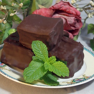 May include: Three chocolate squares stacked on a white and blue patterned plate with a sprig of green mint leaves.