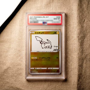 May include: A graded 2021 Pokemon Japanese Pikachu trading card in a clear plastic slab. The card features a minimalist black line drawing of Pikachu by Yu Nagaba, with the text Pikachu, 60 HP, and Japanese characters printed on the card face.