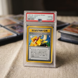 May include: A 1998 Japanese promo Pikachu Illustrator Pokemon card encased in a clear plastic PSA slab. The card features a yellow Pikachu holding a paintbrush and a pen, with the text ILLUSTRATOR and Japanese characters printed on the front.