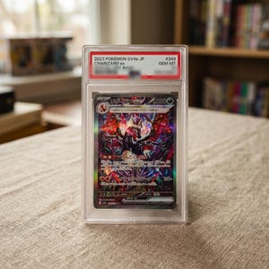 May include: A graded 2023 Pokemon SV4a JP Charizard ex trading card in a clear plastic protective case. The label at the top reads 2023 POKEMON SV4a JP CHARIZARD ex #349 GEM MT. The card features a dark, holographic illustration of Charizard.