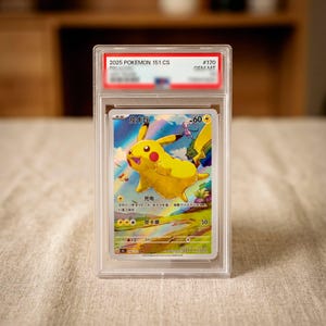 Può includere: Una carta collezionabile Pokemon 151 CS 2025 graduata che raffigura un personaggio Pikachu giallo in un paesaggio con un arcobaleno. La carta è racchiusa in una custodia protettiva in plastica trasparente con un'etichetta rossa e bianca.