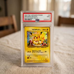 Puede incluir: Una carta coleccionable japonesa promocional Birthday Pikachu de 2001, sellada en una funda de plástico transparente. La carta muestra a un Pikachu amarillo comiendo pastel. La etiqueta superior dice 2001 P.M. JAPANESE PROMO BIRTHDAY PIKACHU #25 MINT.