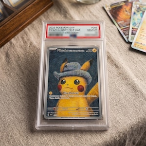 Könnte beinhalten: Eine 2023 Pokemon SVP #085 Pikachu with Grey Felt Hat Sammelkarte in einer transparenten Schutzhülle. Die Karte zeigt ein gelbes Pikachu mit einem grauen Hut vor einem dunkelblauen Hintergrund mit dem Text Pika-Portrait und 60 HP.