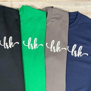 May include: A white ceramic mug with a black handle and the text "But First, Coffee" in a bold, black font. The mug is set against a blurred background, suggesting a cozy setting.