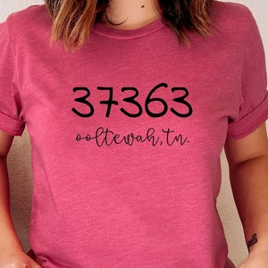 May include: A pink t-shirt with the text "37363 ooltewah, tn." printed in black.