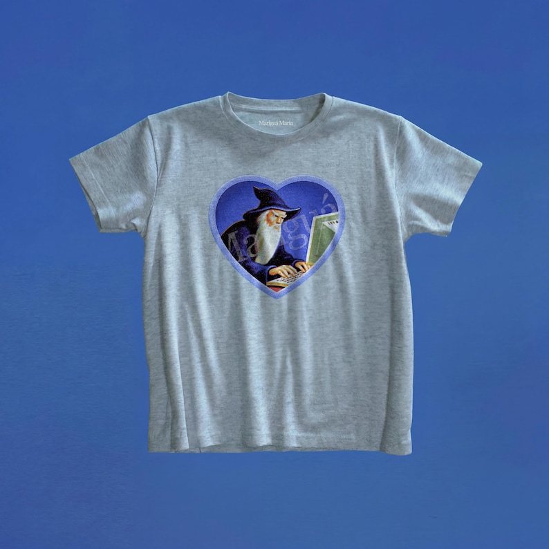 May include: A heather gray short-sleeve t-shirt featuring a central graphic of a wizard with a long white beard and a dark blue pointed hat, typing on a laptop. The graphic is framed within a blue heart shape on the chest of the shirt.