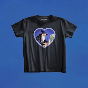 May include: A black short-sleeved t-shirt featuring a central heart-shaped graphic. Inside the heart, a wizard with a long white beard and a blue hat is typing on a computer. The brand name Marigui Maria is printed in white on the inner neck label.