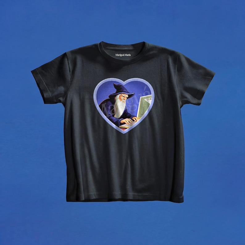 May include: A black short-sleeved t-shirt featuring a central heart-shaped graphic. Inside the heart, a wizard with a long white beard and a blue hat is typing on a computer. The brand name Marigui Maria is printed in white on the inner neck label.
