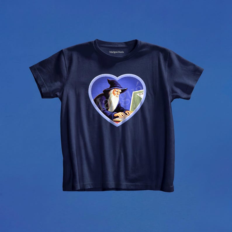 May include: A navy blue short-sleeved t-shirt featuring a central heart-shaped graphic. Inside the heart, a wizard with a long white beard and a dark blue pointed hat is typing on a computer. The brand name Marigai Maria is printed on the inner neck.