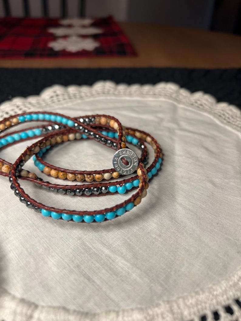 May include: Wrap bracelets with turquoise, brown, and gray beads. The bracelets are made of leather and have a metal clasp. The bracelets are displayed on a white lace doily.