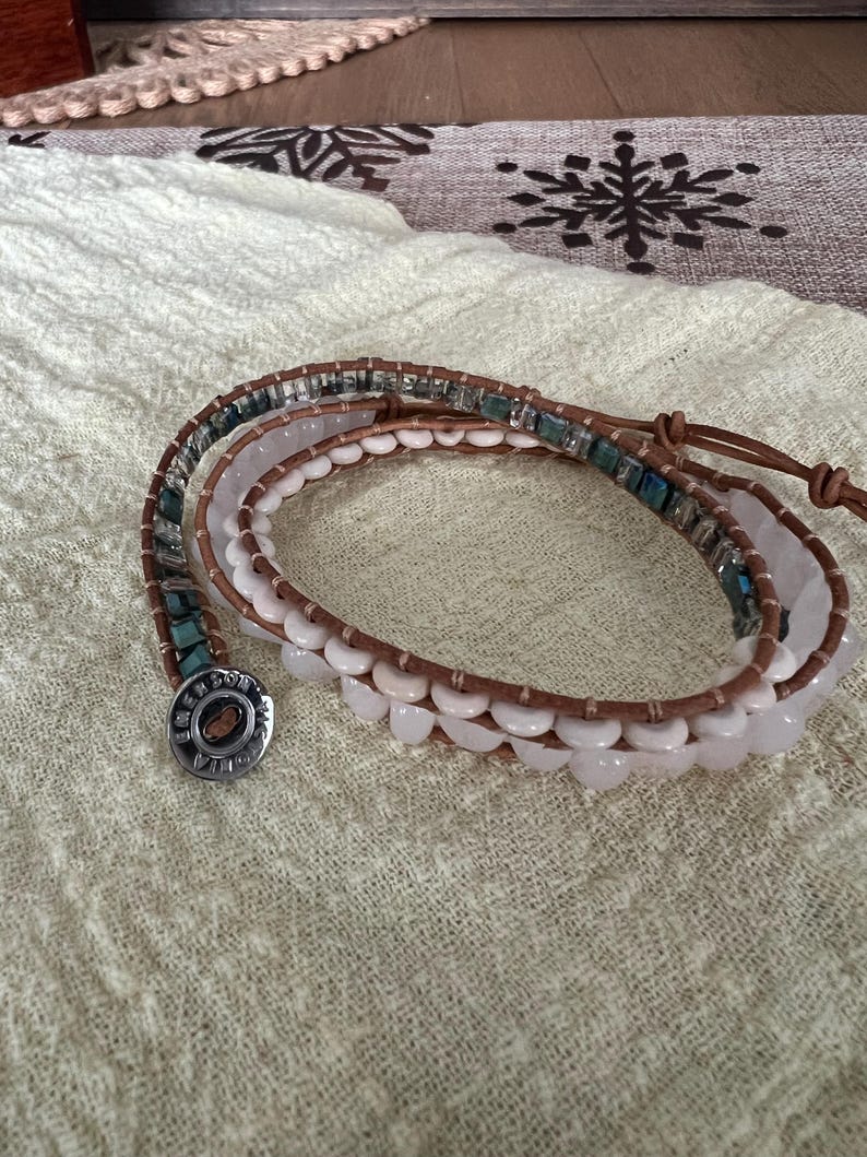 May include: Wrap bracelet featuring a combination of light brown leather, white and pink beads, and turquoise accents. The bracelet has a silver-toned button clasp. The design is suitable for everyday wear.