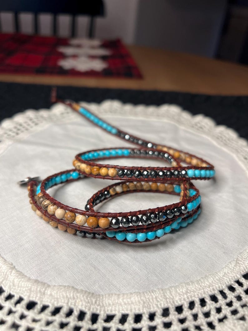 May include: Wrap bracelet featuring brown leather and various beads. The bracelet includes turquoise, brown, and black beads. The design is a multi-strand wrap style, suitable for a bohemian or casual aesthetic.
