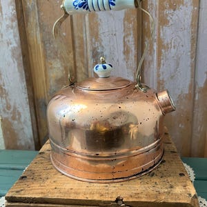 A vintage copper tea kettle featuring a blue and white Delft-style porcelain handle and lid knob