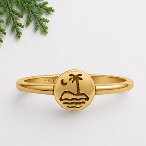 Könnte beinhalten: Ein goldfarbener Ring mit einer runden Platte, die ein eingraviertes Motiv einer Palme auf einer Insel unter einer Mondsichel zeigt. Auf der Innenseite des Rings ist deutlich der Schriftzug S925 eingeprägt, der auf Sterlingsilber hinweist.