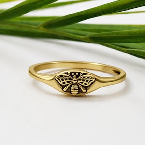Könnte beinhalten: Ein goldfarbener Ring mit einem zentralen Bienenmotiv, detaillierten Flügelmustern und einem gestreiften Körper. Auf der Innenseite des Rings ist deutlich der Text S925 eingeprägt, der die Metallzusammensetzung des Schmuckstücks angibt.