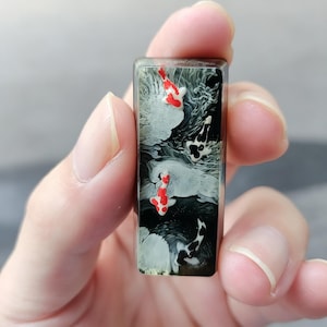 May include: A rectangular resin keycap featuring a detailed artistic design of multiple koi fish swimming in dark water. The scene includes two prominent red and white koi, along with black and white patterned koi, set against swirling white and black ink-like patterns.