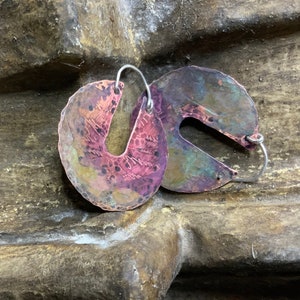 May include: A pair of copper earrings with a hammered finish. The earrings are a crescent shape with a silver wire hoop.