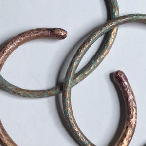 May include: Three hammered copper bracelets with a turquoise patina finish. The bracelets are stacked on top of each other.