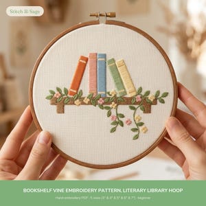 May include: A circular wooden embroidery hoop containing white fabric with a hand-stitched design of five colorful books on a brown shelf, accented by green vines and small pink and yellow flowers. The text Stitch & Sage is visible.