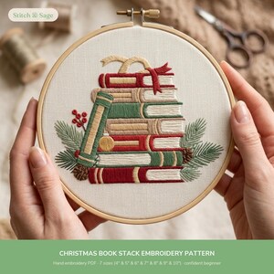 Può includere: Un telaio da ricamo circolare in legno contenente un pannello in tessuto con un disegno ricamato a mano di una pila di libri in rosso, verde e beige. I libri sono decorati con un nastro rosso, rami di pino, bacche e un piccolo ornamento.